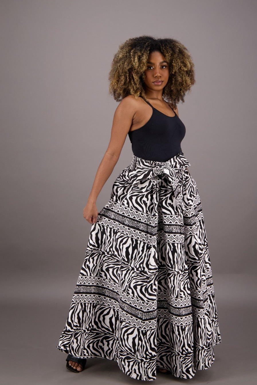 A woman wearing a dashiki-print maxi cotton skirt with a bold zebra and geometric print, featuring a high elasticized full waistband and attached bow tie belt.